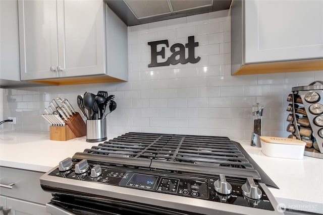 kitchen with stainless steel gas stove, white cabinets, light countertops, and decorative backsplash