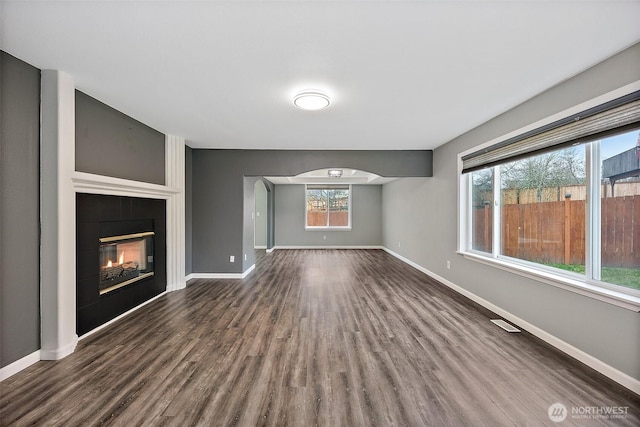 unfurnished living room with visible vents, baseboards, arched walkways, dark wood-style floors, and a fireplace