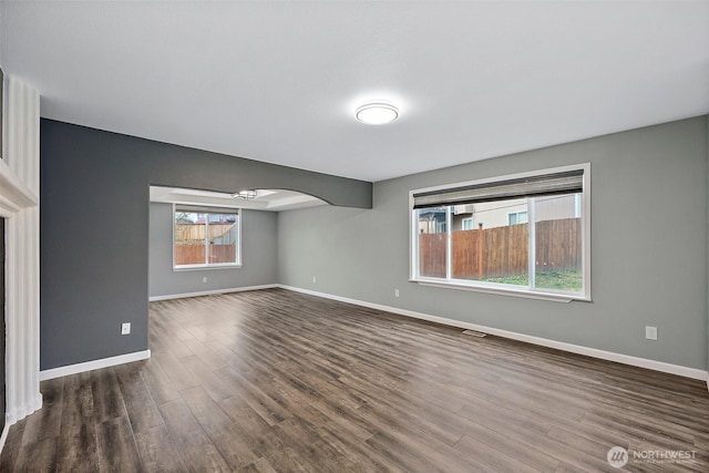 unfurnished room with arched walkways, dark wood-style flooring, visible vents, and baseboards