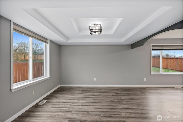 unfurnished room with baseboards, visible vents, a raised ceiling, and dark wood-type flooring