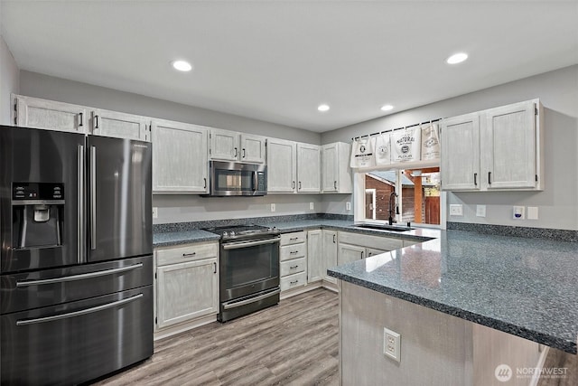 kitchen with recessed lighting, a peninsula, a sink, light wood-style floors, and appliances with stainless steel finishes