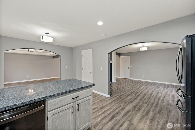 kitchen featuring light wood finished floors, baseboards, arched walkways, dishwasher, and freestanding refrigerator