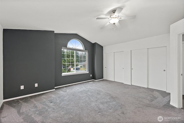 unfurnished bedroom featuring baseboards, a ceiling fan, lofted ceiling, carpet floors, and two closets