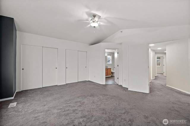 unfurnished bedroom featuring visible vents, connected bathroom, vaulted ceiling, carpet floors, and two closets