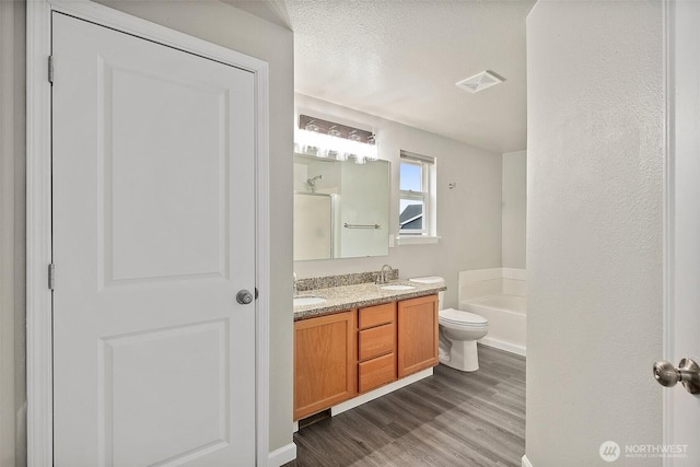 bathroom featuring a garden tub, double vanity, visible vents, a sink, and wood finished floors