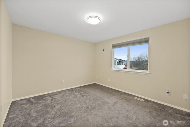 empty room featuring dark colored carpet, visible vents, and baseboards