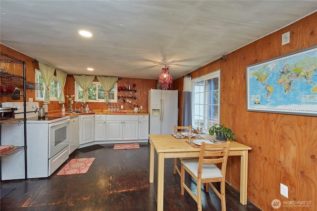 kitchen featuring white cabinetry, white appliances, wood walls, and a sink