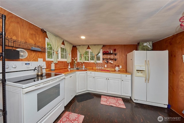 kitchen with dark wood-style floors, wood walls, white appliances, and white cabinetry