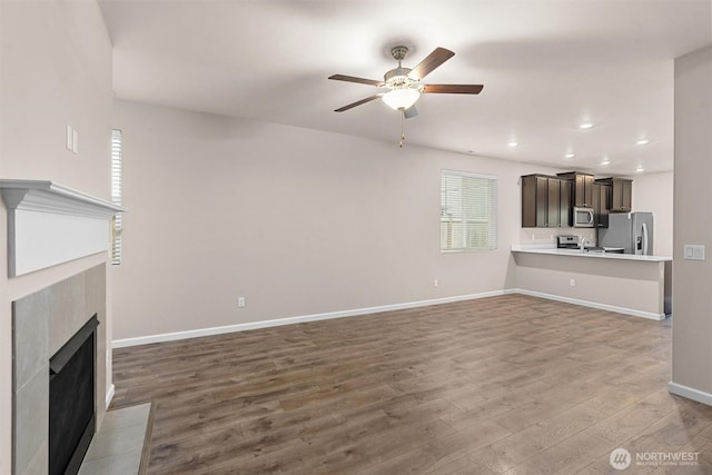 unfurnished living room featuring wood finished floors, recessed lighting, a fireplace, baseboards, and ceiling fan