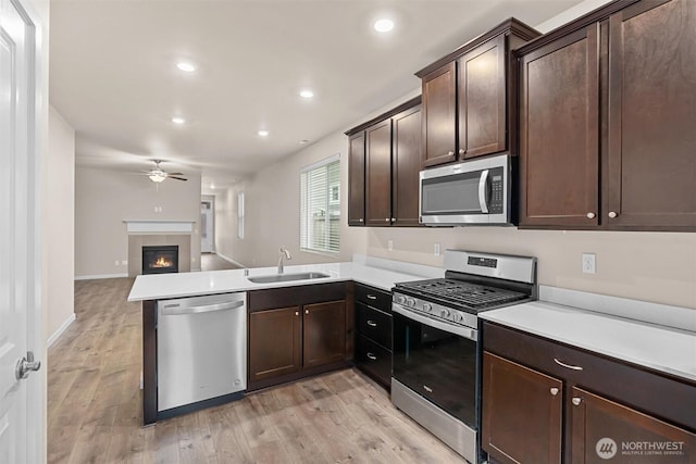 kitchen with open floor plan, a tile fireplace, appliances with stainless steel finishes, a peninsula, and a sink