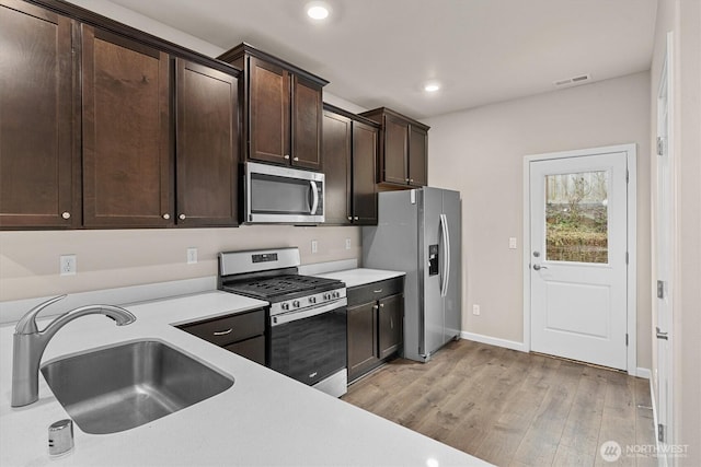 kitchen featuring a sink, stainless steel appliances, light wood finished floors, dark brown cabinets, and light countertops