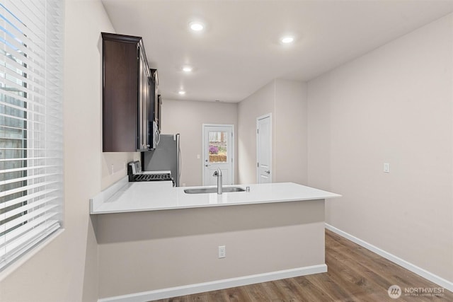 kitchen featuring a sink, a peninsula, light countertops, baseboards, and dark brown cabinets