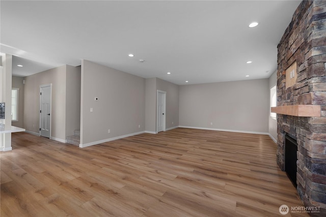 unfurnished living room featuring light wood finished floors, a stone fireplace, baseboards, and recessed lighting