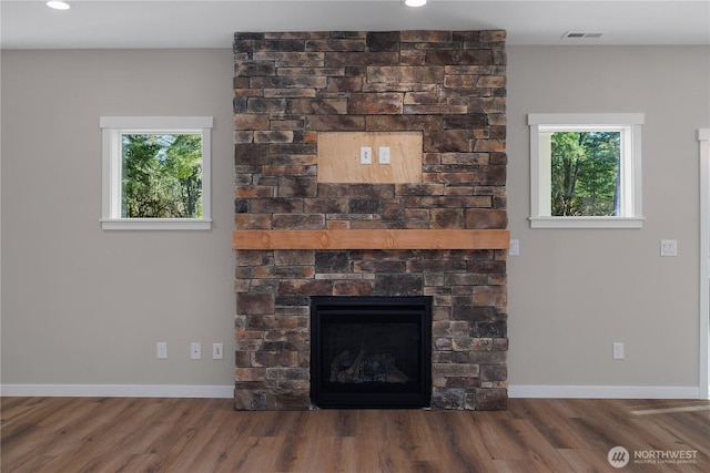 interior details with baseboards, visible vents, wood finished floors, and a stone fireplace