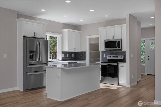 kitchen with appliances with stainless steel finishes, a kitchen island, wood finished floors, and white cabinets