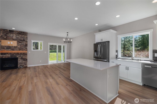 kitchen featuring white cabinets, open floor plan, stainless steel appliances, a fireplace, and a sink