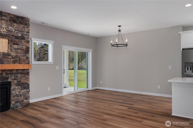 unfurnished dining area featuring visible vents, an inviting chandelier, a stone fireplace, wood finished floors, and baseboards