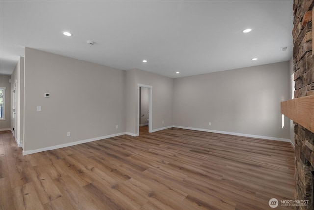 unfurnished living room featuring baseboards, light wood-type flooring, a fireplace, and recessed lighting