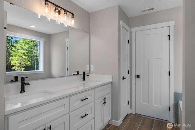 full bath with double vanity, visible vents, a sink, and wood finish floors