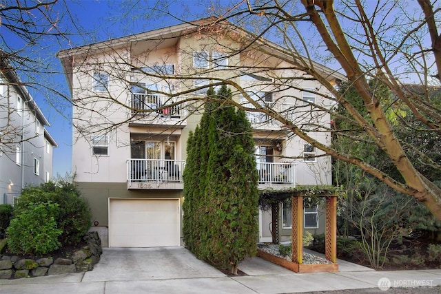 view of front of house with concrete driveway, a balcony, an attached garage, and stucco siding