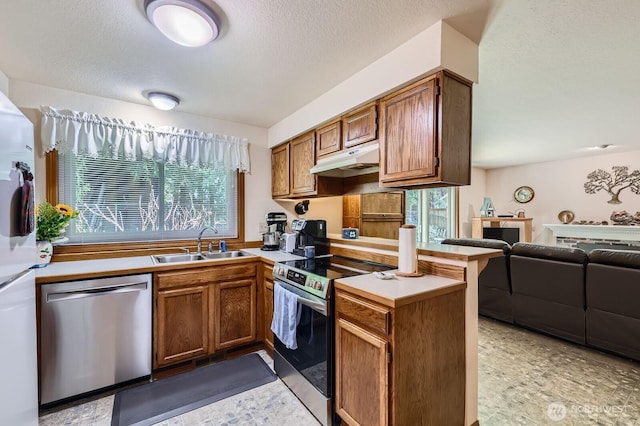 kitchen featuring under cabinet range hood, a sink, open floor plan, appliances with stainless steel finishes, and a peninsula