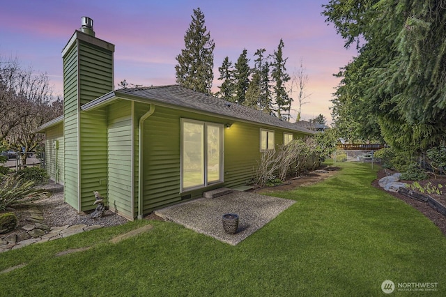 back of property at dusk with a patio, a yard, and a chimney