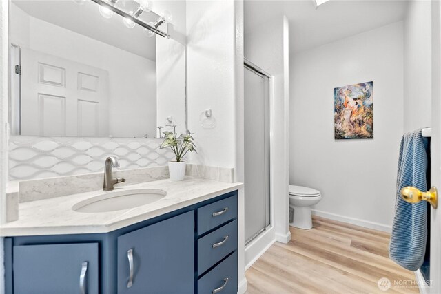 bathroom featuring vanity, toilet, wood finished floors, and a stall shower