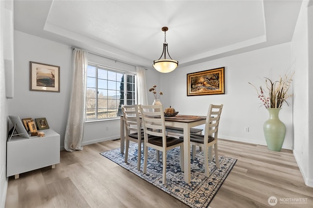 dining space with a tray ceiling, light wood-style floors, and baseboards