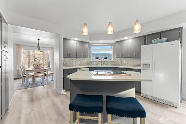 kitchen featuring light wood finished floors, a healthy amount of sunlight, light countertops, white refrigerator with ice dispenser, and black electric cooktop