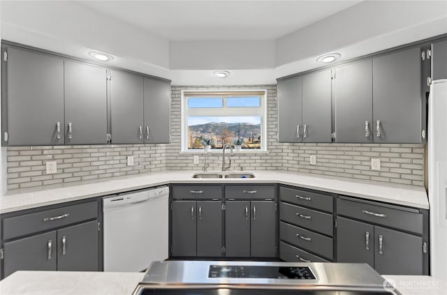 kitchen with gray cabinetry, a sink, backsplash, white dishwasher, and light countertops