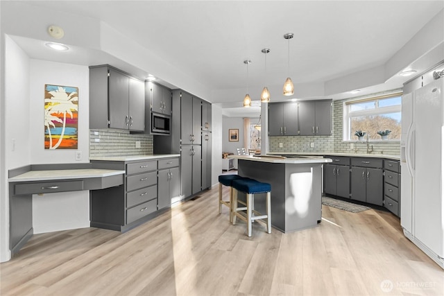 kitchen with a kitchen island, gray cabinets, white fridge with ice dispenser, stainless steel microwave, and light wood-type flooring