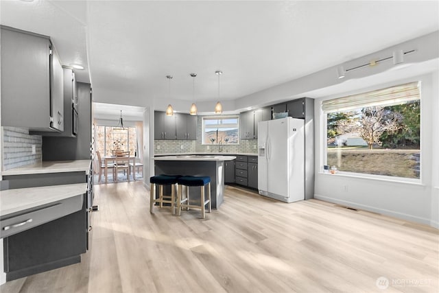 kitchen with plenty of natural light, white fridge with ice dispenser, gray cabinetry, and light wood finished floors