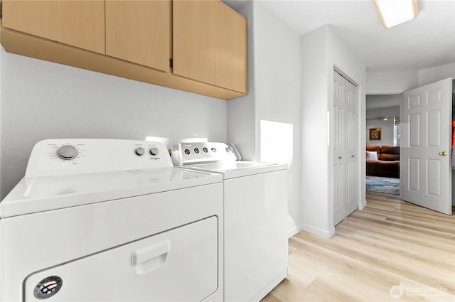 clothes washing area with baseboards, cabinet space, light wood-type flooring, and washer and clothes dryer