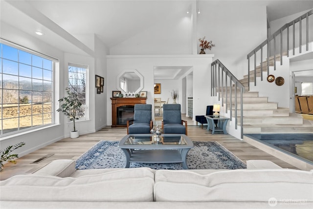 living area with a glass covered fireplace, stairway, high vaulted ceiling, and wood finished floors