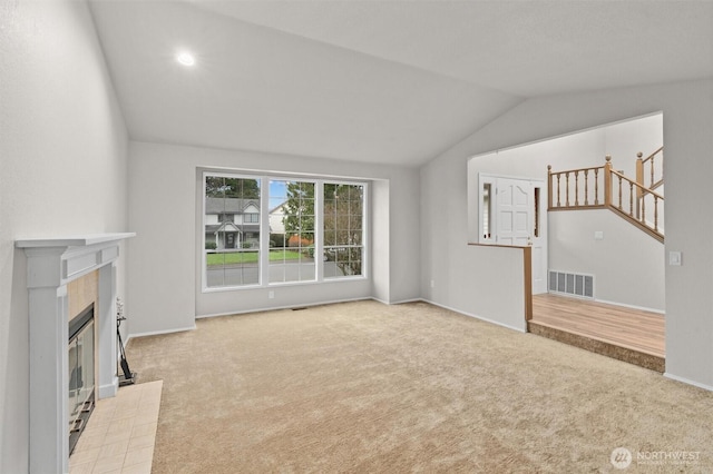 unfurnished living room with visible vents, a tiled fireplace, stairway, carpet floors, and lofted ceiling