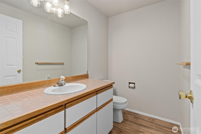 bathroom with vanity, toilet, wood finished floors, and baseboards