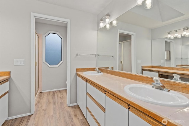 full bath featuring double vanity, wood finished floors, a stall shower, and a sink