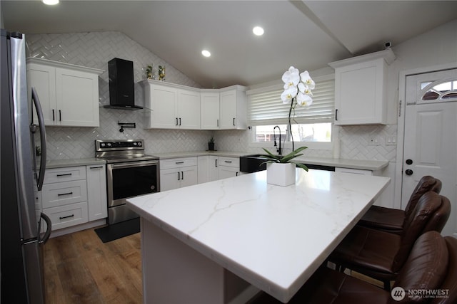 kitchen with stainless steel appliances, white cabinetry, vaulted ceiling, and wall chimney range hood