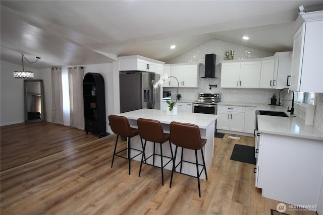 kitchen featuring lofted ceiling, appliances with stainless steel finishes, a sink, light wood-type flooring, and wall chimney exhaust hood