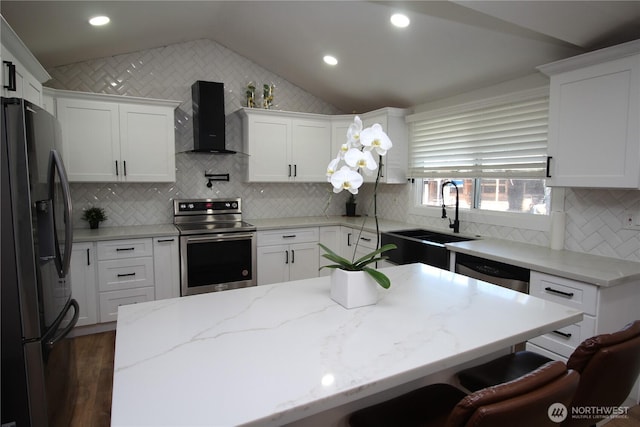 kitchen featuring a sink, vaulted ceiling, appliances with stainless steel finishes, wall chimney exhaust hood, and a kitchen bar