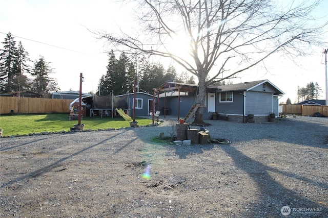 view of front of home with a trampoline, gravel driveway, a fenced backyard, and a front yard