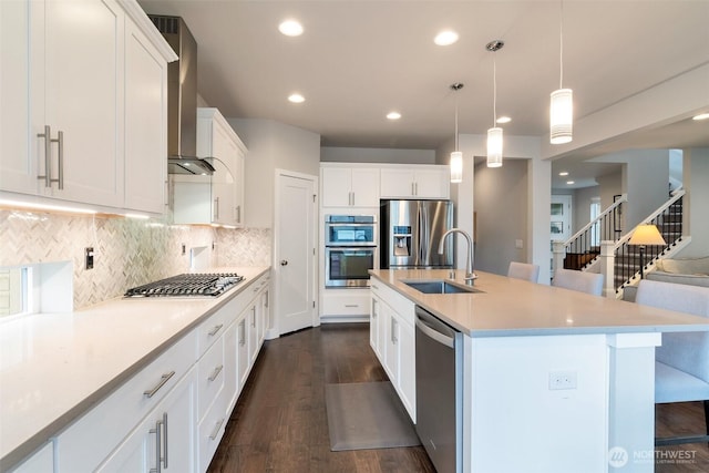 kitchen with dark wood-type flooring, wall chimney range hood, light countertops, appliances with stainless steel finishes, and a sink