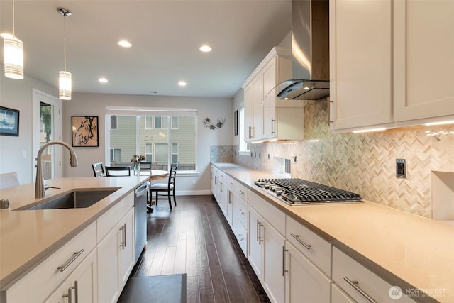 kitchen with backsplash, light countertops, appliances with stainless steel finishes, wall chimney exhaust hood, and a sink