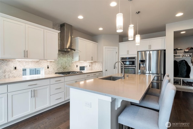 kitchen with dark wood-style floors, a sink, white cabinets, appliances with stainless steel finishes, and wall chimney exhaust hood