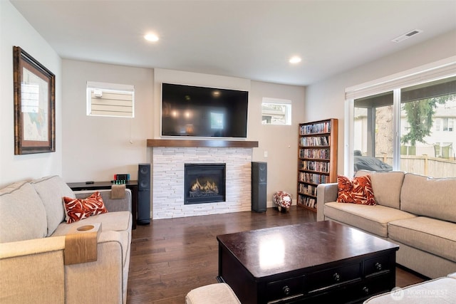 living area featuring visible vents, baseboards, recessed lighting, dark wood-style flooring, and a stone fireplace