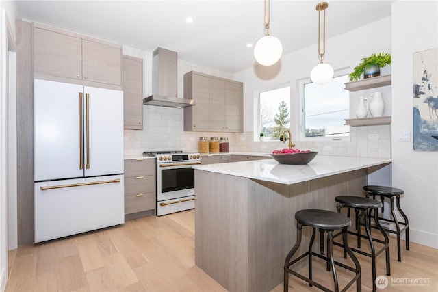 kitchen with white appliances, a breakfast bar area, a peninsula, light wood-style flooring, and wall chimney exhaust hood