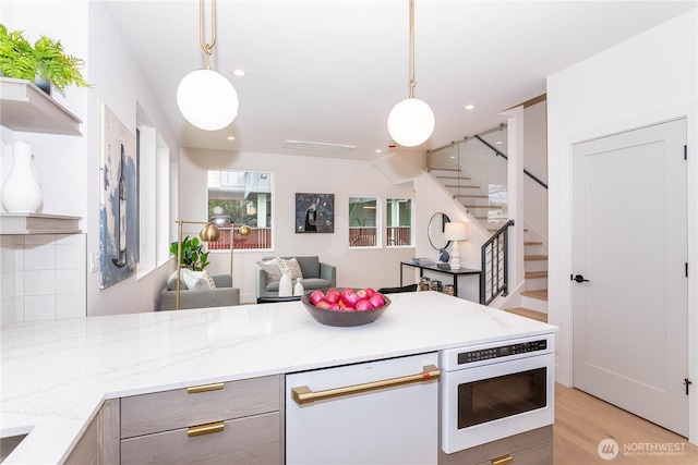 kitchen with light wood-type flooring, pendant lighting, light stone counters, open shelves, and a peninsula