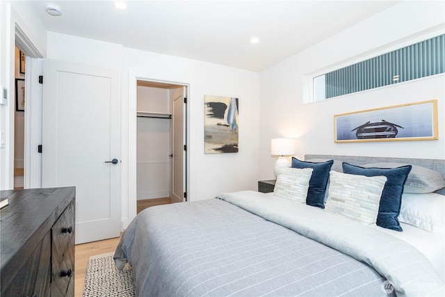 bedroom with recessed lighting, a walk in closet, and light wood-style floors