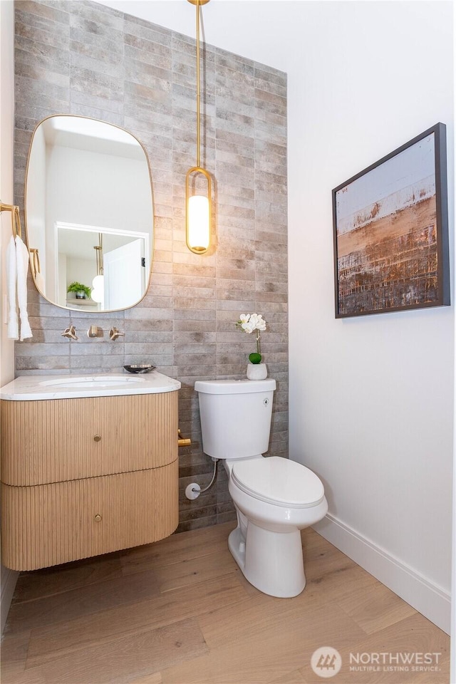 bathroom with toilet, vanity, baseboards, and wood finished floors