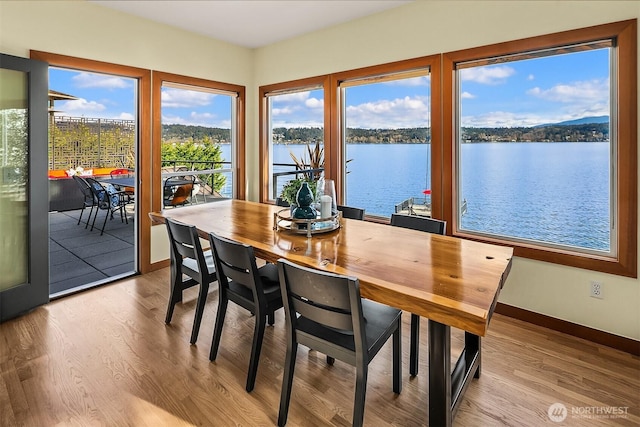 dining area with baseboards, a water view, and wood finished floors